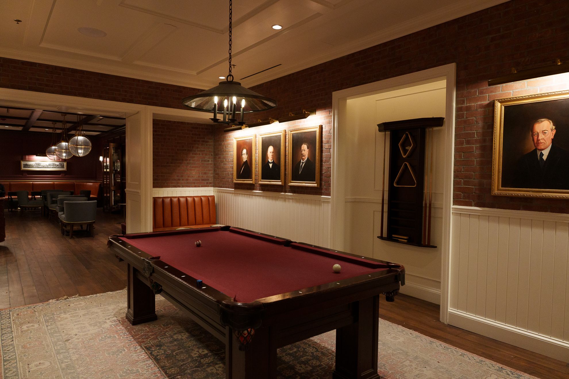 A billiard table beneath brick arches and hung portraits in a hotel game room