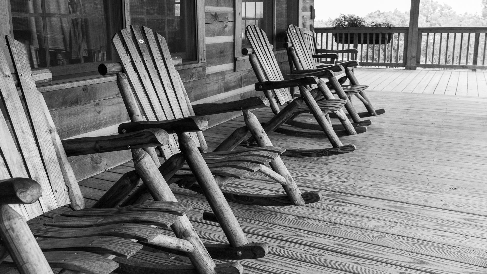 A row of wooden rocking chairs along a cabin porch, black and white