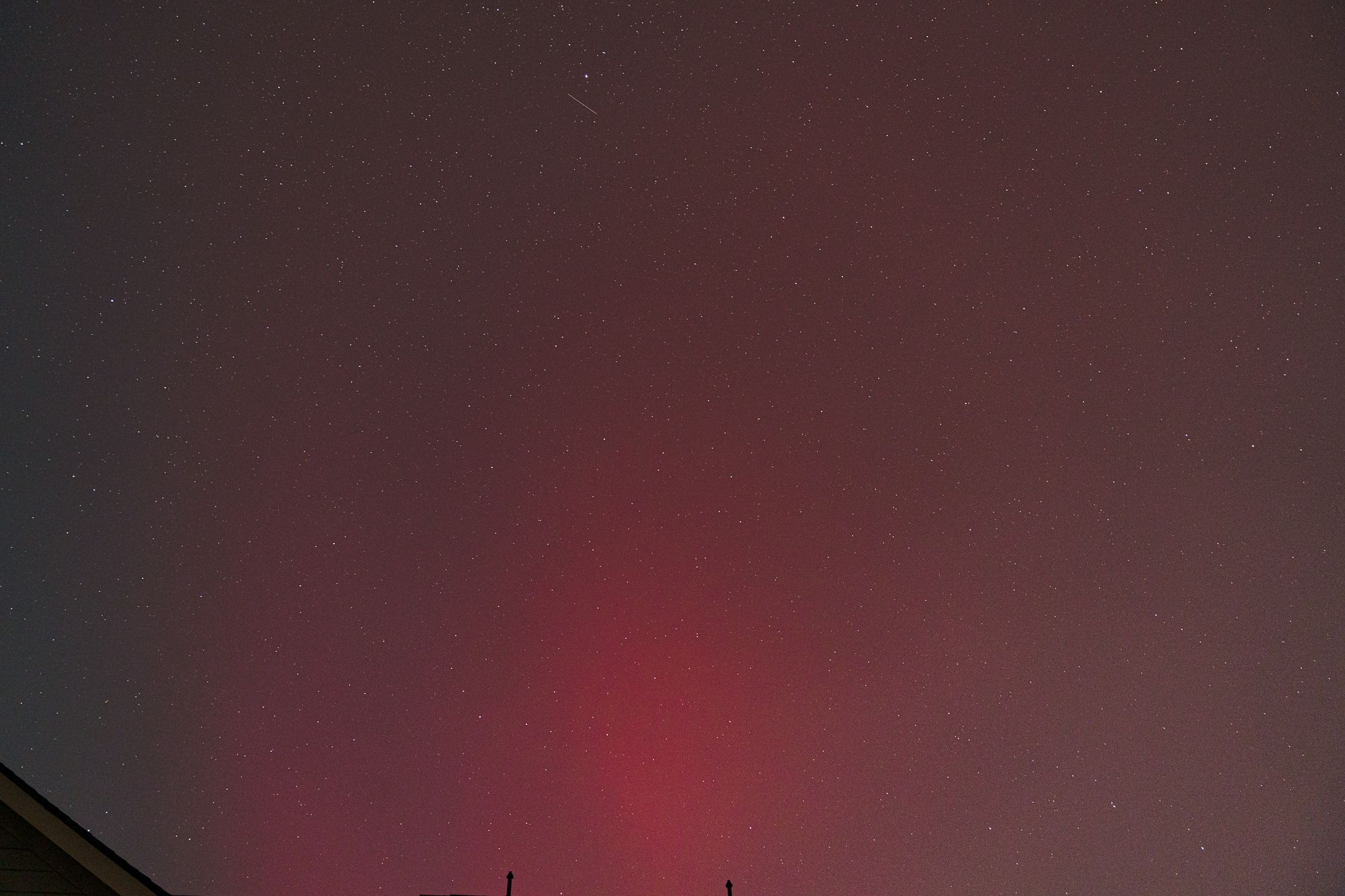 A faint red aurora and stars over a dark rooftop