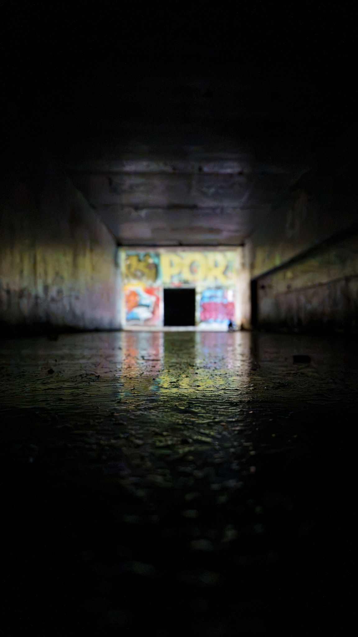 Graffiti glowing at the far end of a wet pedestrian tunnel