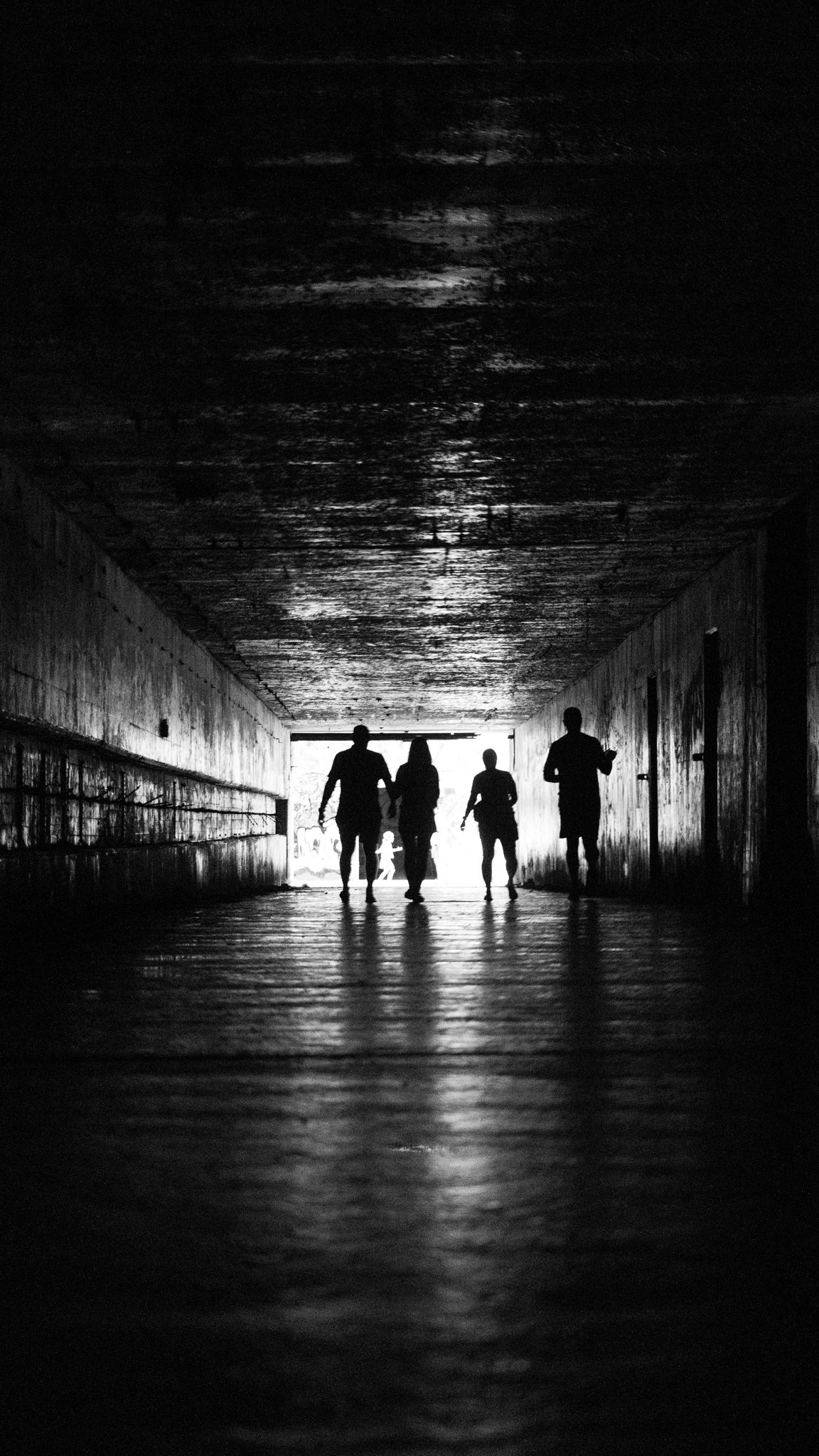 Four silhouettes walking a dark tunnel toward the light, black and white