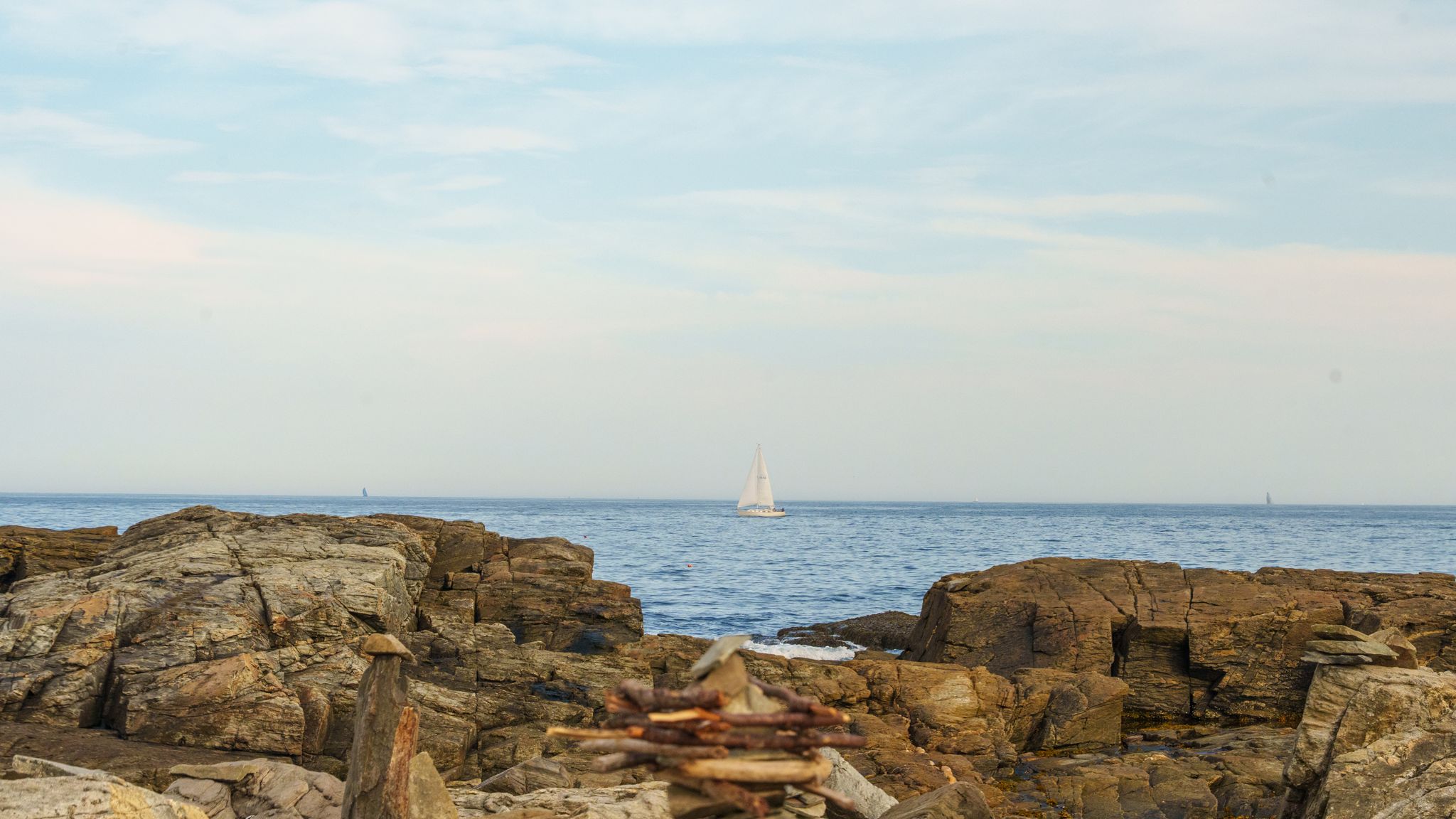 A lone white sail on the horizon beyond dark rocks