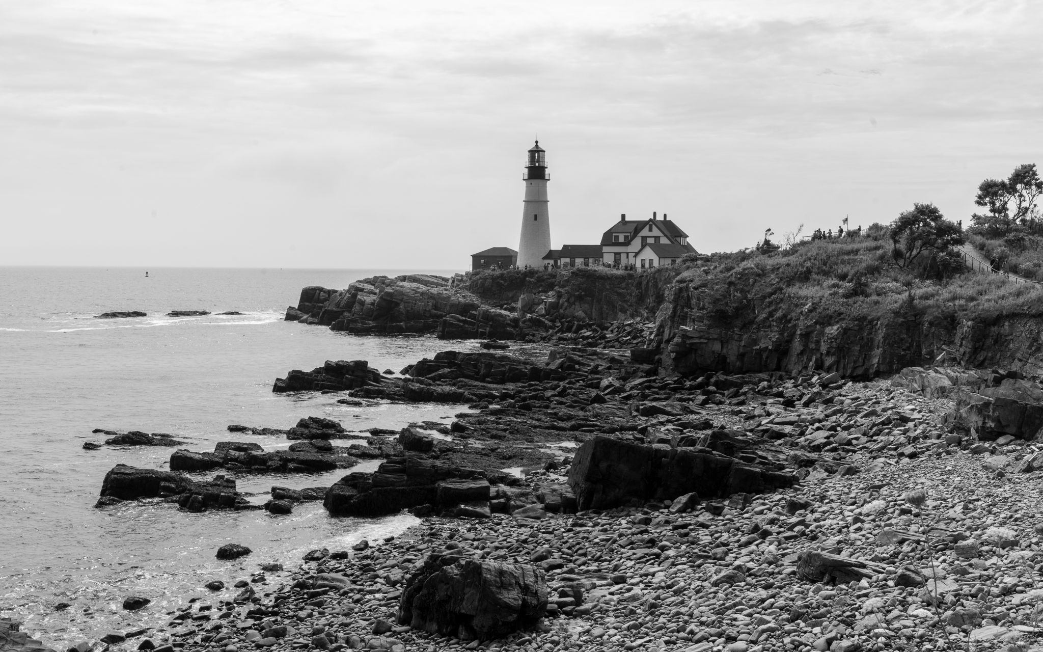 Portland Head Light above a cobble beach, black and white
