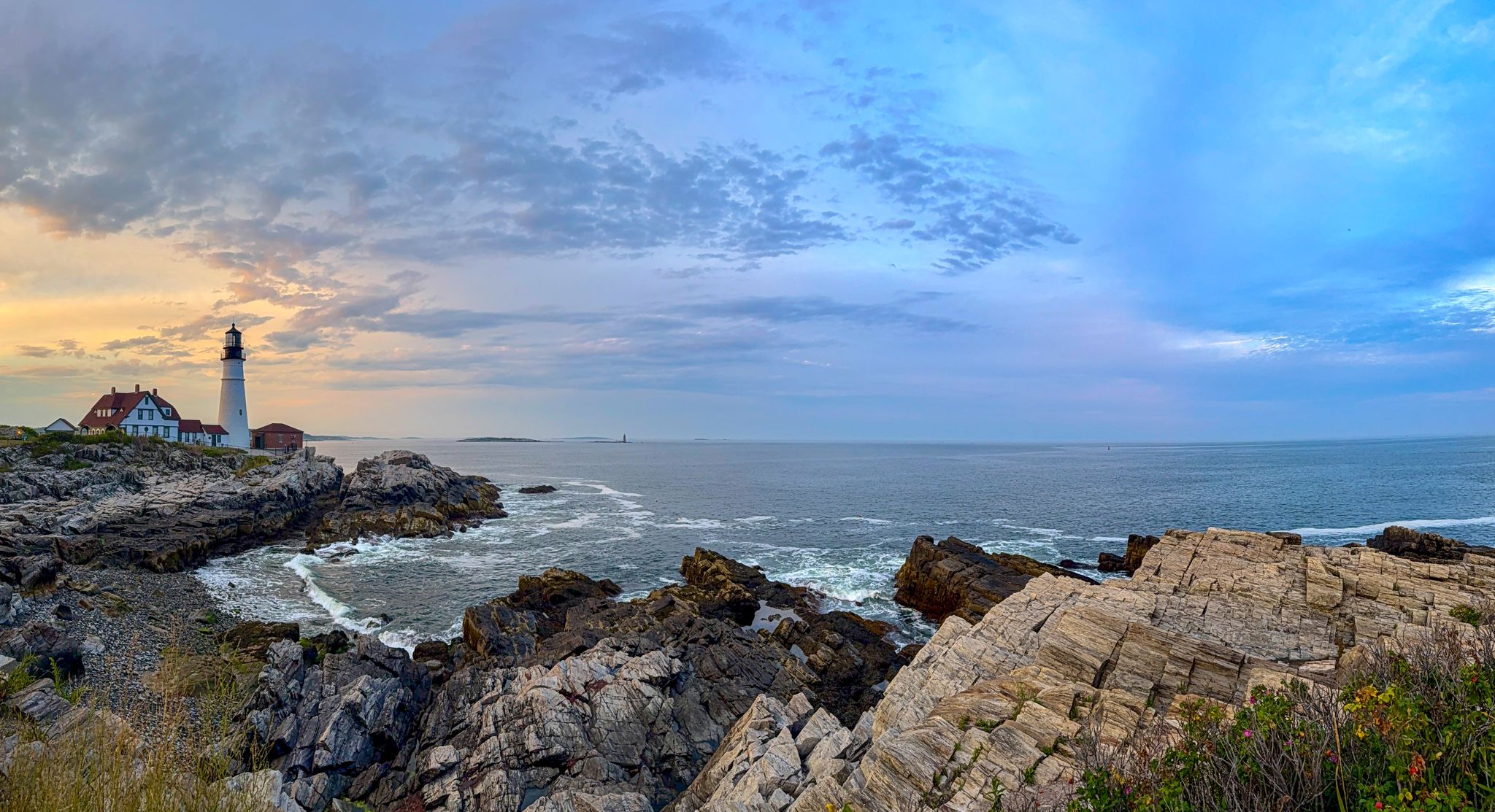 Portland Head Light across pink granite ledges under a broad sky
